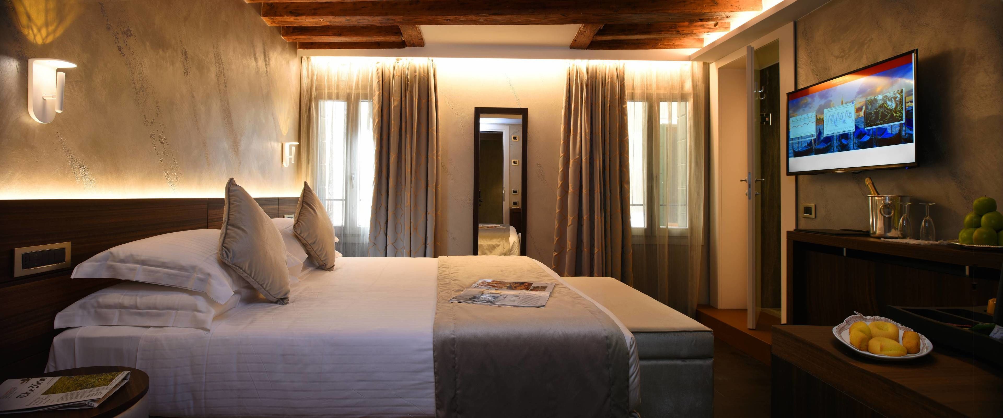 A hotel room with a bed, a television, a small table with fruits, and a newspaper.