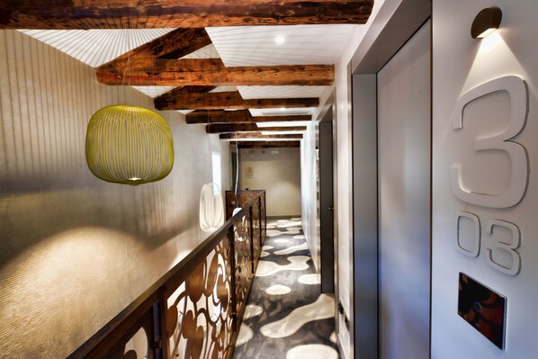 A modern hallway with exposed wooden beams, a patterned floor, and a number '3' sign.