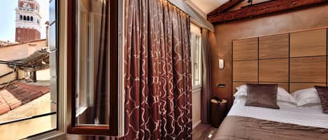 A hotel room with a large window, a bed with a brown bedspread, and a wooden headboard.