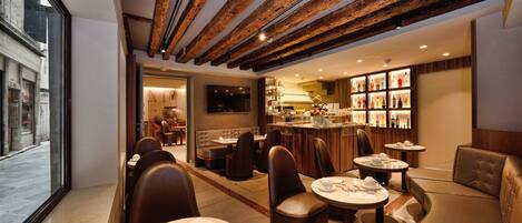 A modern restaurant with wooden ceiling beams, round tables, and leather seating.