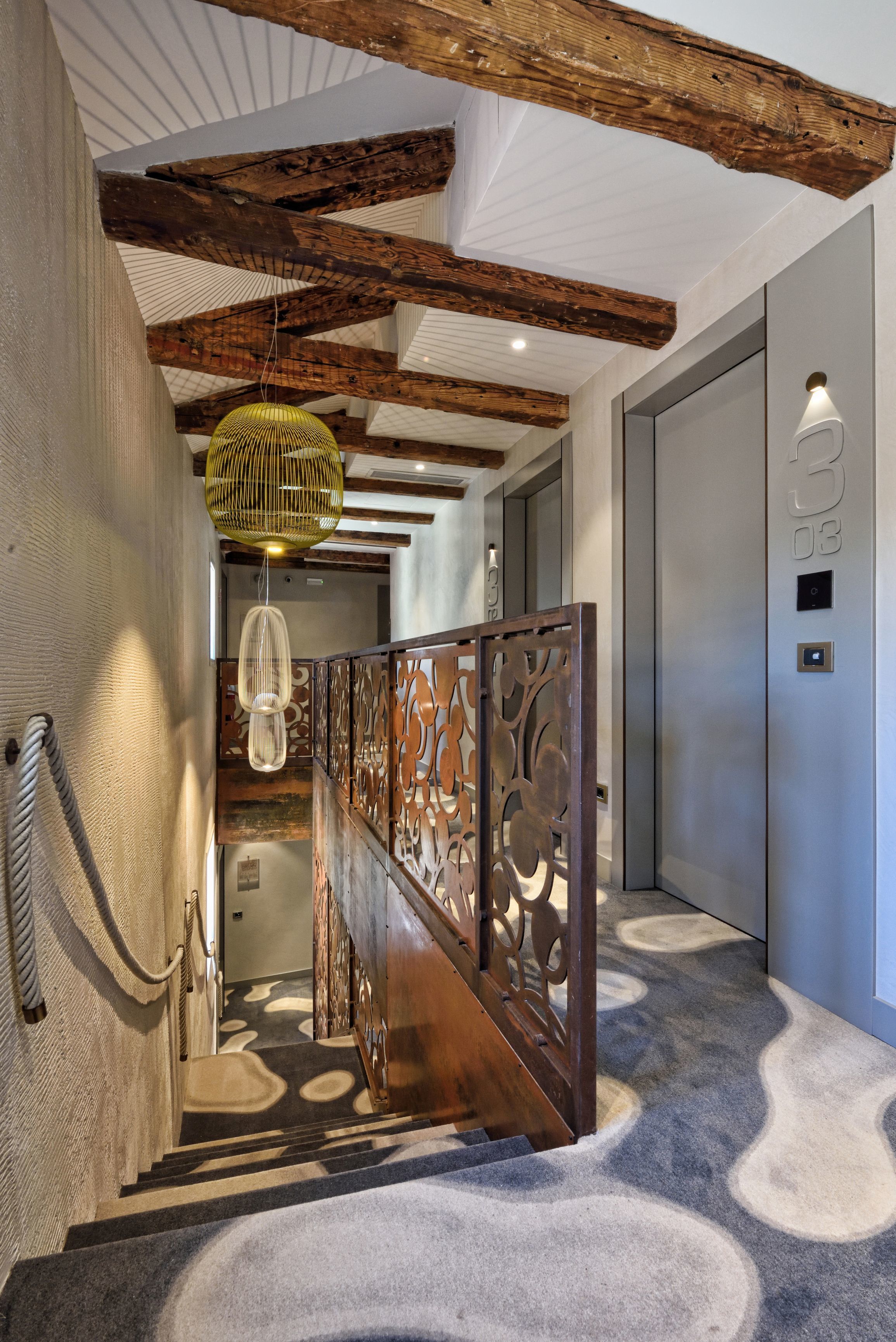 A staircase with a patterned carpet, wooden railing, and a hanging light fixture.