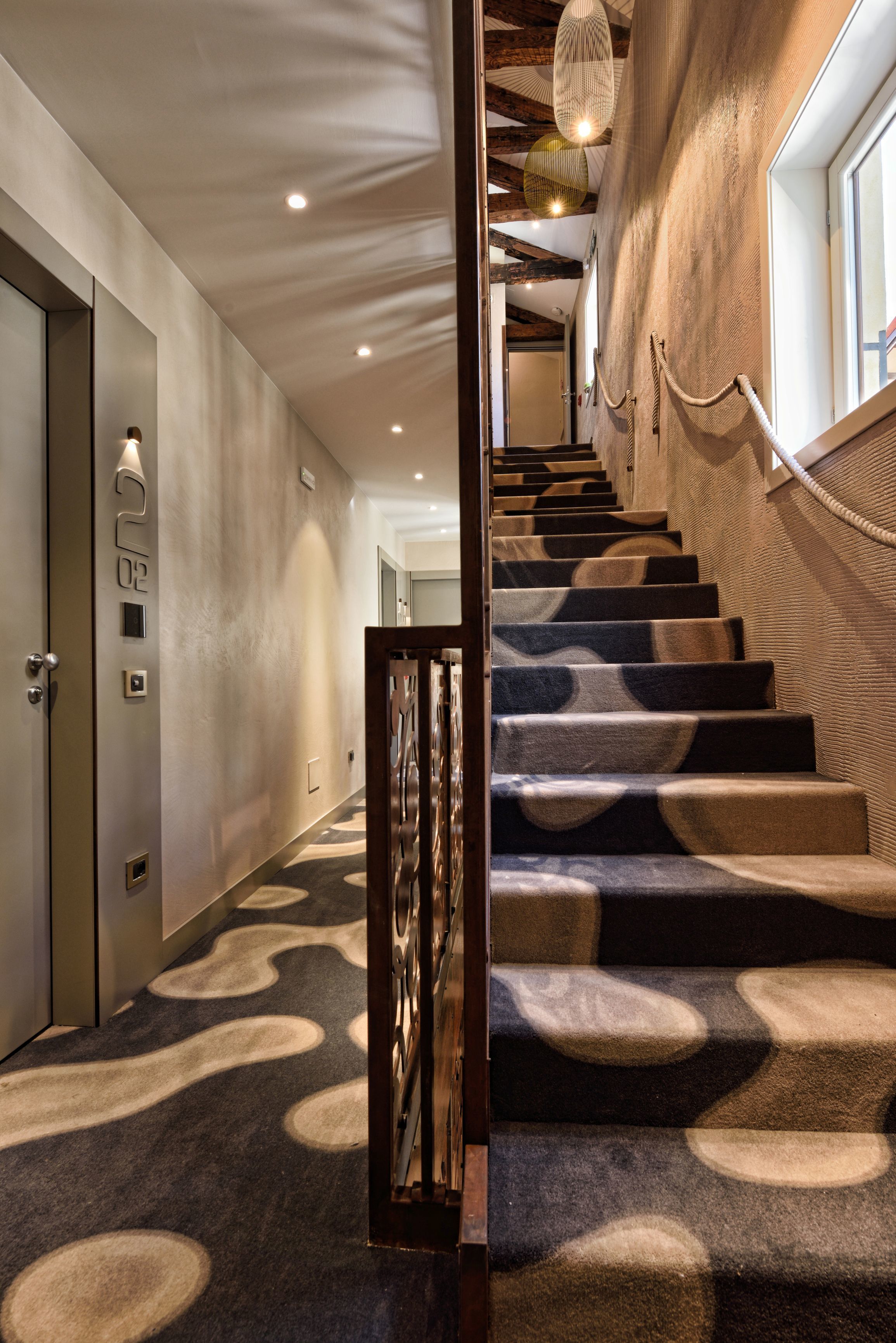 A staircase with a patterned carpet, a wooden handrail, and a wall with a textured finish.