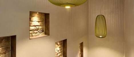 A staircase with a wooden handrail, a green hanging light fixture, and stone wall accents.
