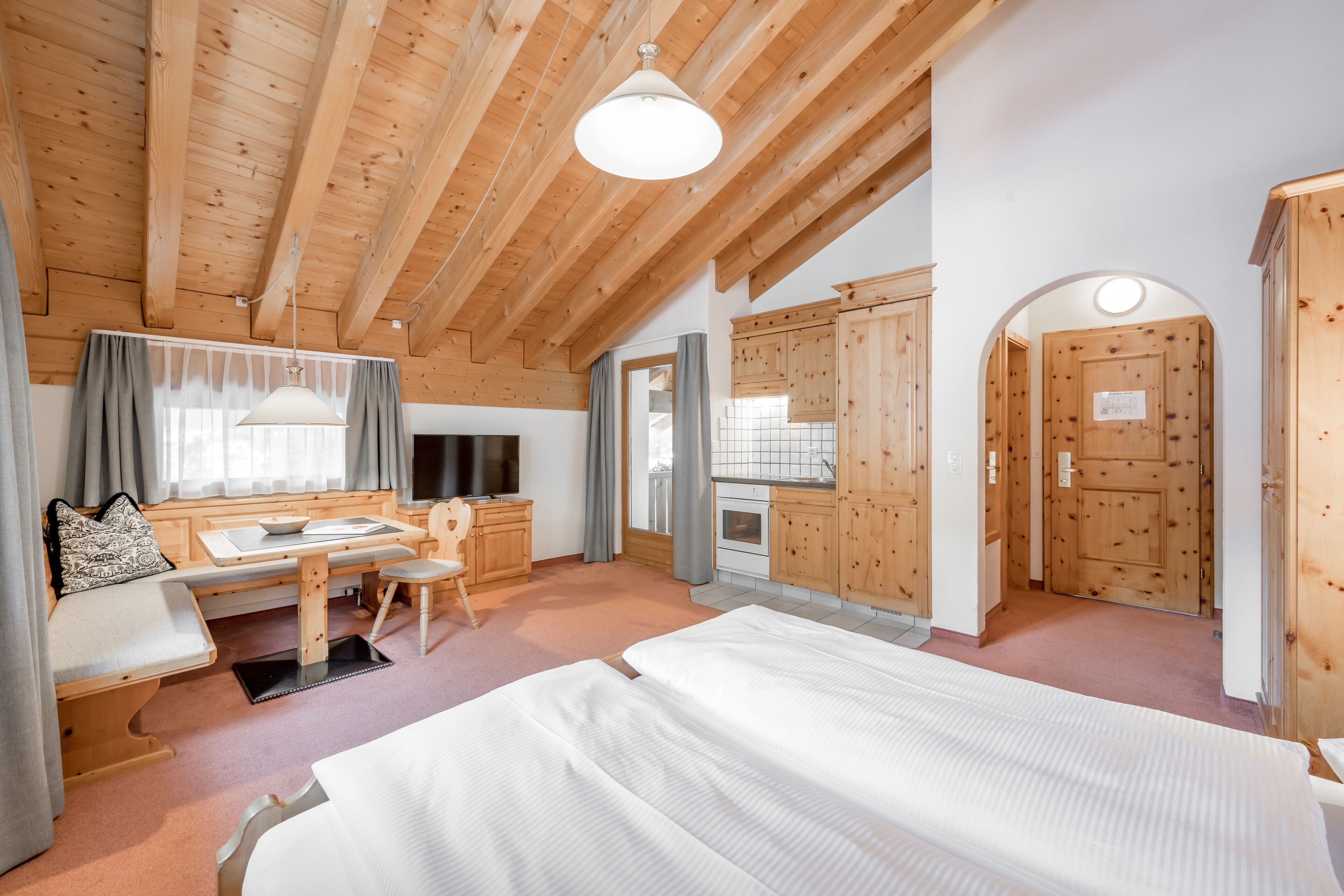 Una habitación acogedora con techo de madera, cama, escritorio con silla y ventana con cortinas.