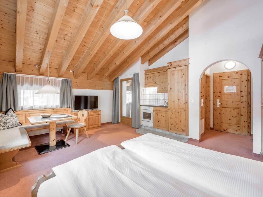 Una habitación acogedora con techo de madera, cama, escritorio con silla y ventana con cortinas.