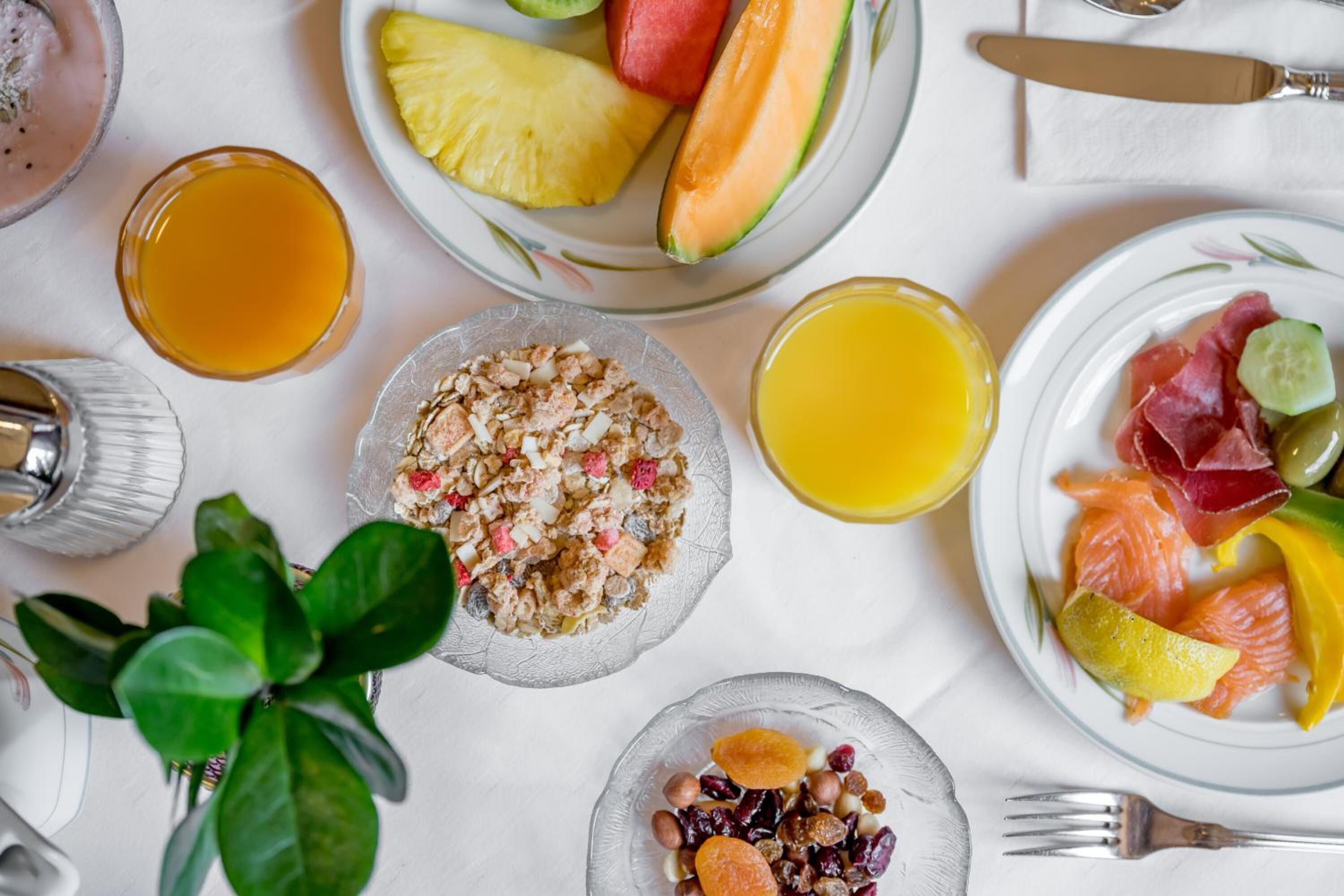 A breakfast setting with plates of fruits, a bowl of cereal, and glasses of orange juice.