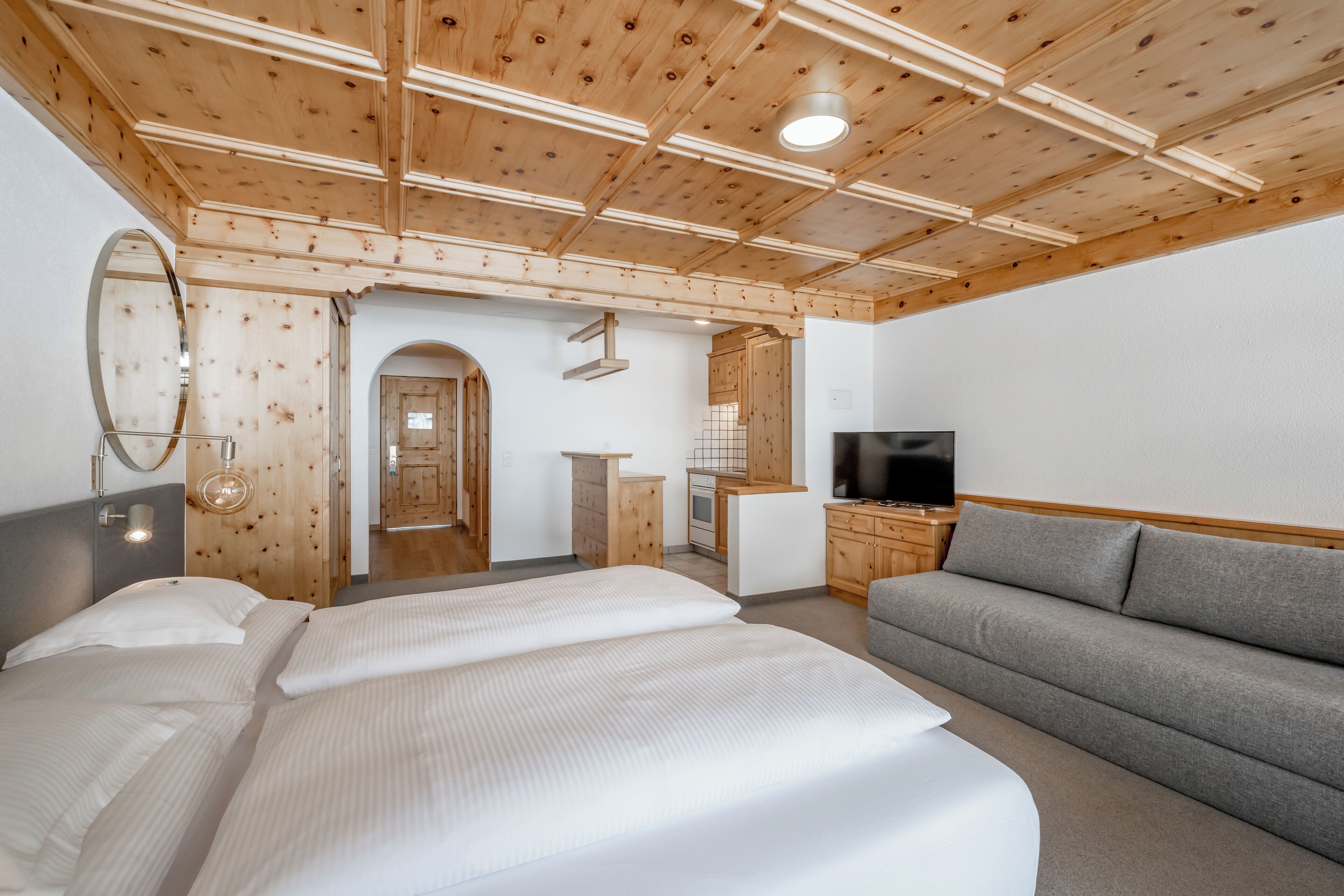 Habitación de hotel con techo de madera, una cama, un sofá, un televisor y una kitchenette.