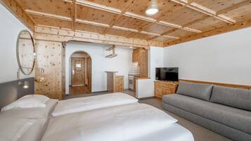 Habitación de hotel con techo de madera, una cama, un sofá, un televisor y una kitchenette.