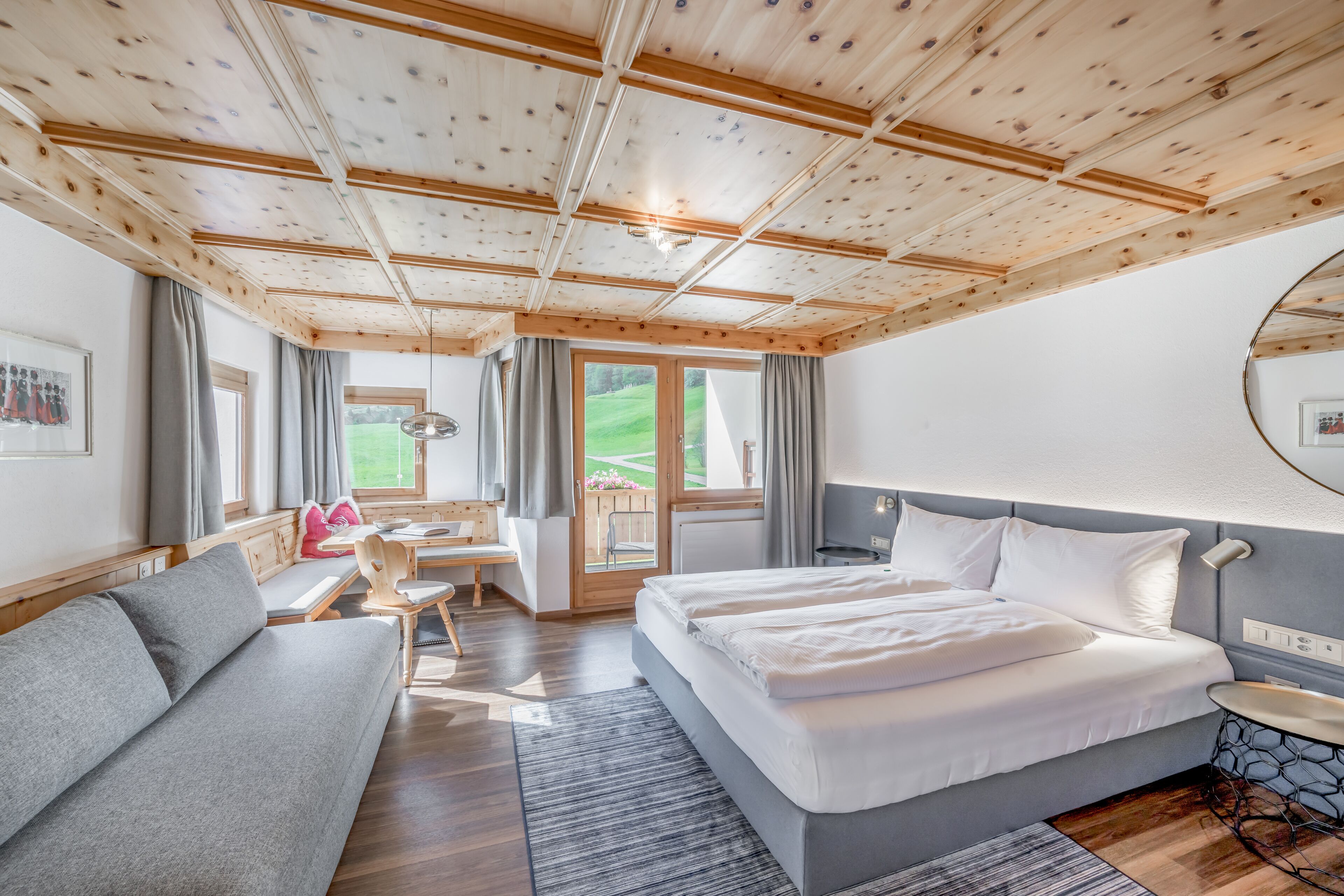 Een moderne hotelkamer met een houten plafond, een groot bed, een zithoek, een bureau en uitzicht op het omliggende landschap.