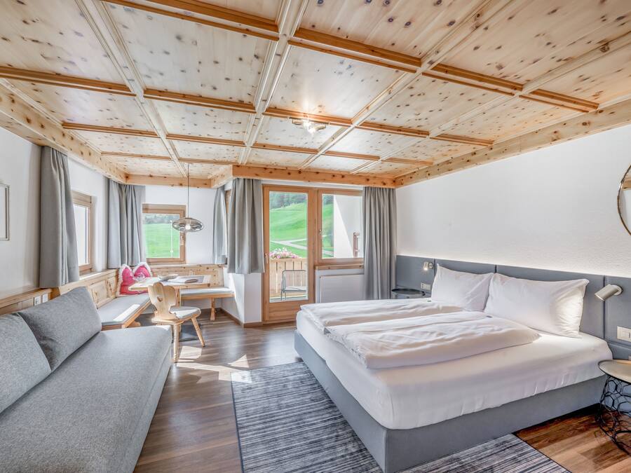 Een moderne hotelkamer met een houten plafond, een groot bed, een zithoek, een bureau en uitzicht op het omliggende landschap.