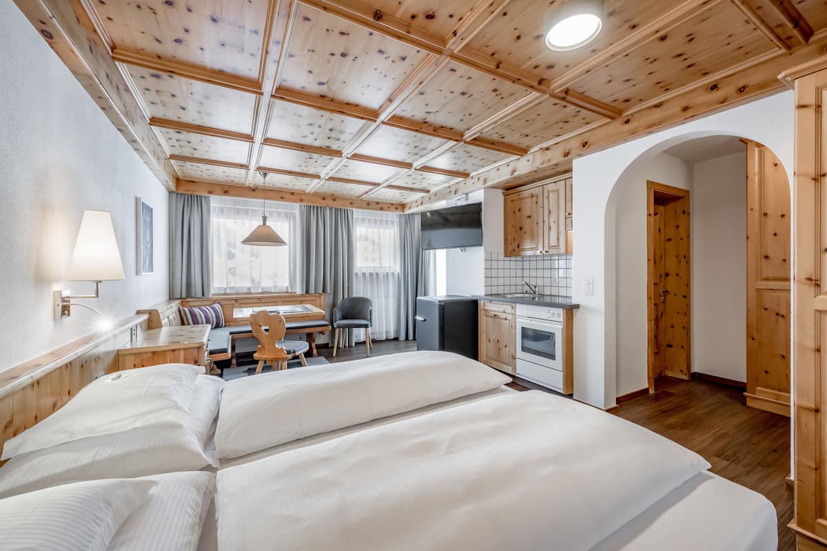 Ein Zimmer mit Holzboden, einem Bett, einem Schreibtisch, einem Stuhl, einer kleinen Küchenzeile und einem Badezimmer.