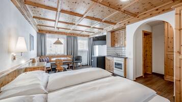A room with a wooden ceiling, a bed, a desk, a chair, a small kitchenette, and a bathroom.