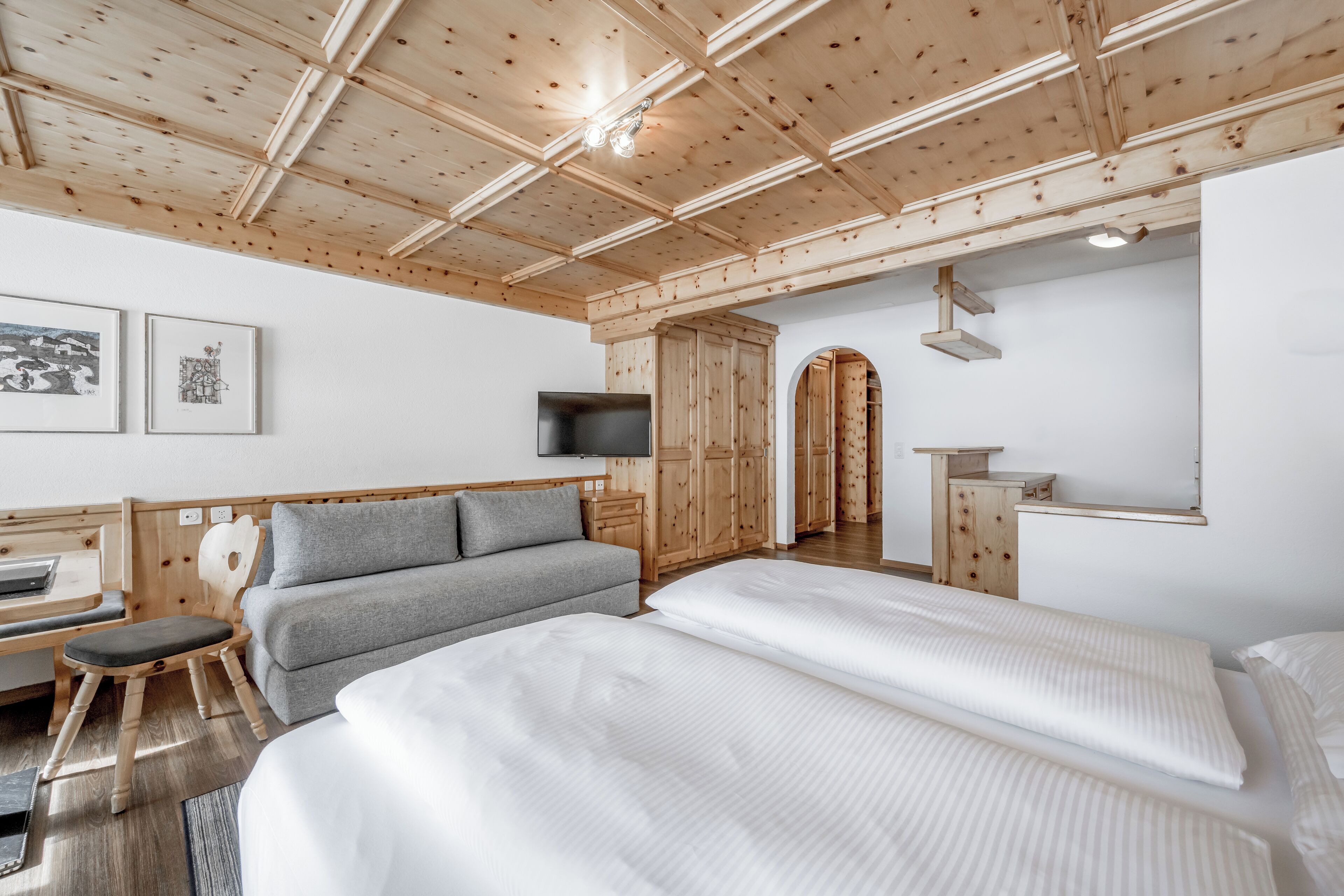A modern hotel room with a wooden ceiling, a sofa, a bed, a desk, and a TV.