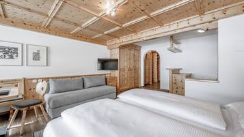 A modern hotel room with a wooden ceiling, a sofa, a bed, a desk, and a TV.