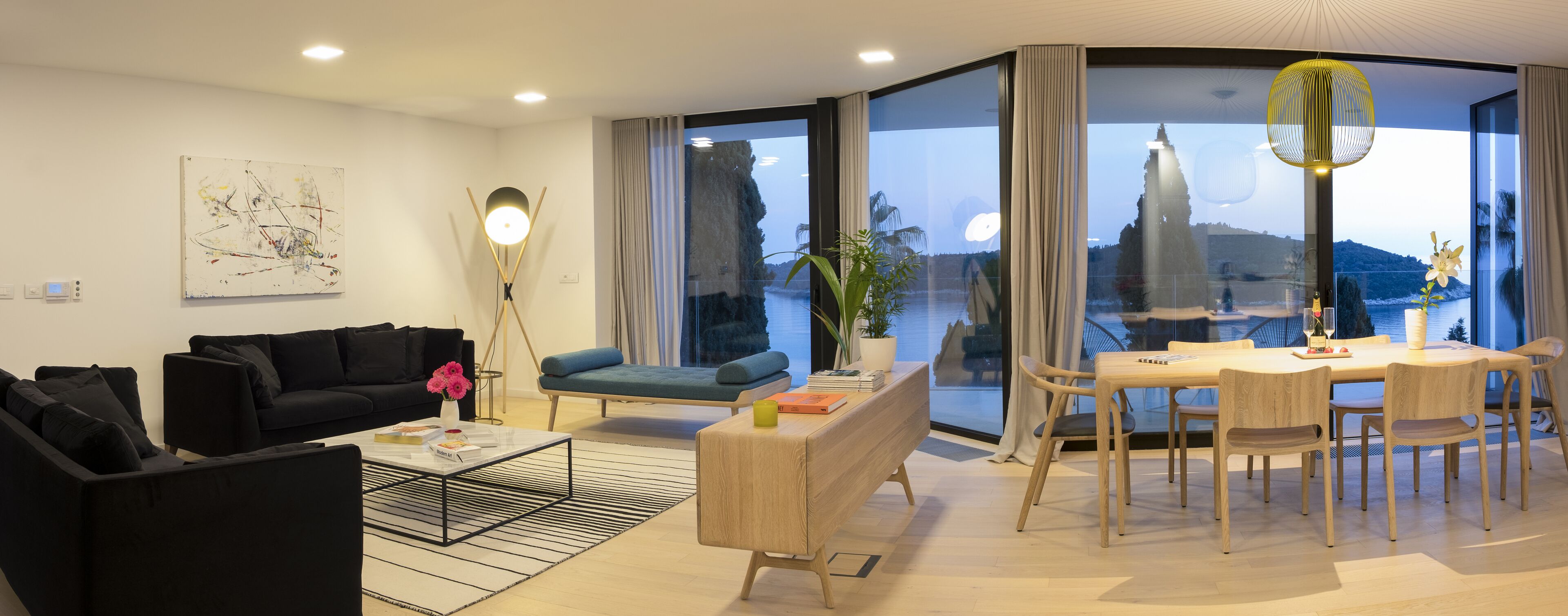 Een moderne woonkamer met een zwarte bank, een blauwe fauteuil, een salontafel en een eethoek met houten stoelen en een tafel.