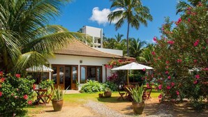 A two-story house with a white exterior and a tiled roof, surrounded by lush greenery and palm trees. - Pousada San Giovanni (Japaratinga)