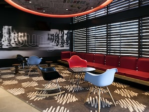 Ein modernes Interieur mit einem roten Sofa, blauen Stühlen, einem kleinen Tisch und einem gemusterten Teppich.