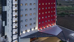Un hotel moderno con una fachada llamativa en rojo y blanco, numerosas ventanas y una entrada cubierta.