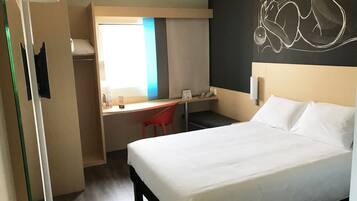 A hotel room with a bed, a desk, and a chair. There is a window with a view of the outside.
