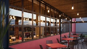 Un comedor interior con mesas y sillas, ventanas amplias y lámparas colgantes.