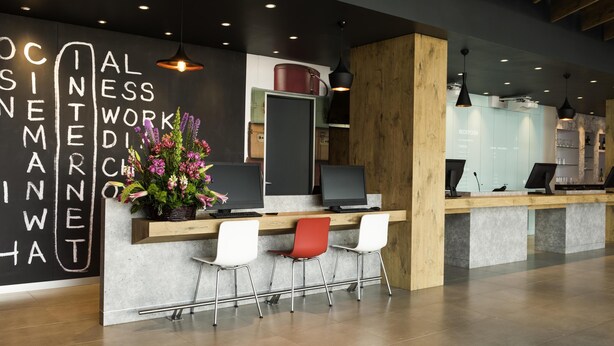 Un mostrador de recepción de diseño moderno, con una pizarra que tiene texto blanco, una planta en maceta y dos monitores de ordenador.