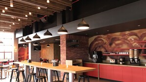 Un café moderno con una barra de madera larga, taburetes negros y armarios rojos.