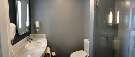 A modern bathroom with a marble sink, a toilet, and a glass shower enclosure.