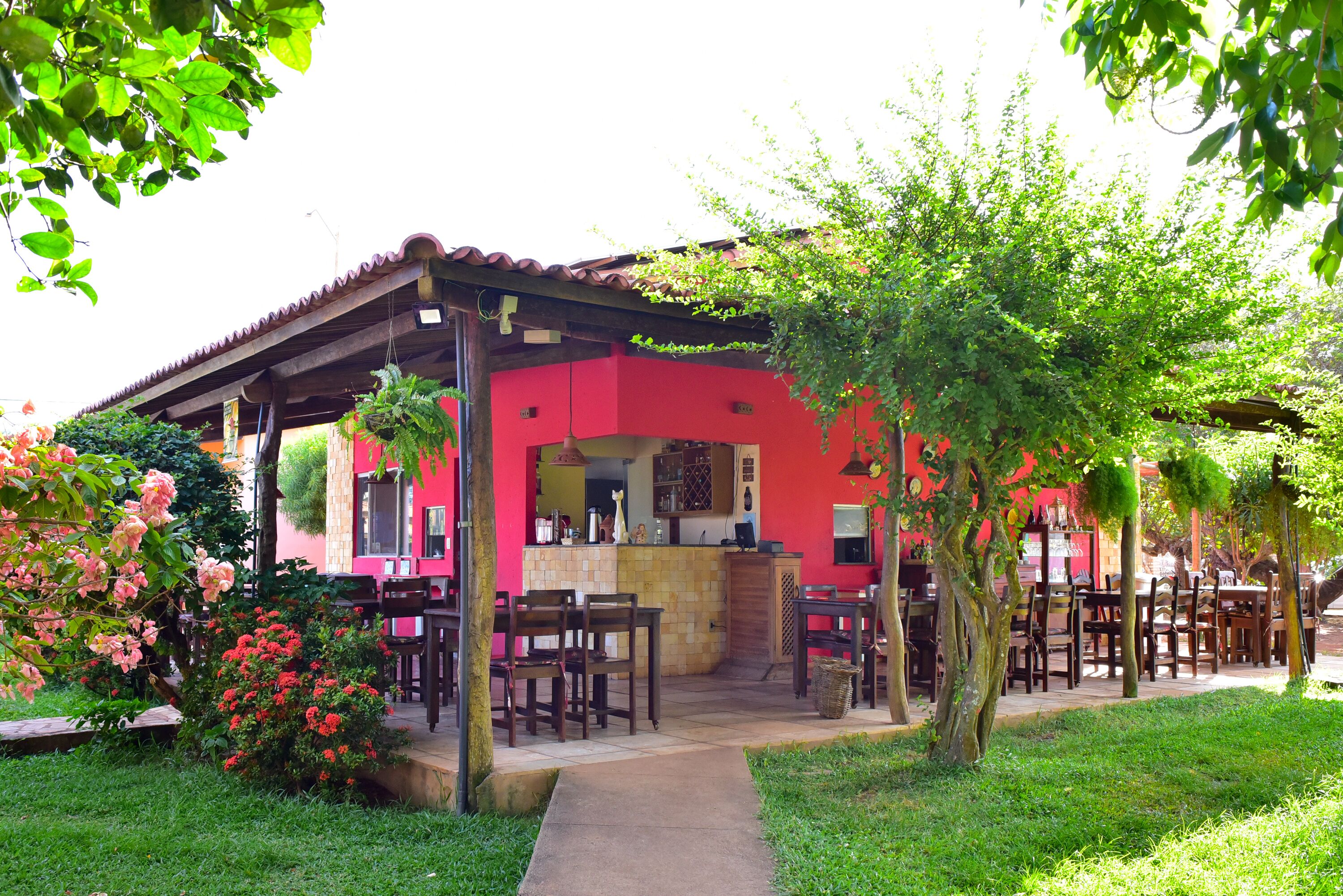 Un edificio rojo con un patio cubierto, asientos al aire libre y un jardín con flores.