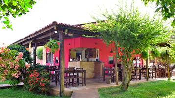 Un edificio rojo con un patio cubierto, asientos al aire libre y un jardín con flores.