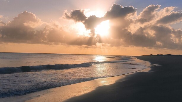 Eine Strandansicht, auf der die Sonne am Horizont untergeht und Sand und Wasser in warmes Licht taucht.