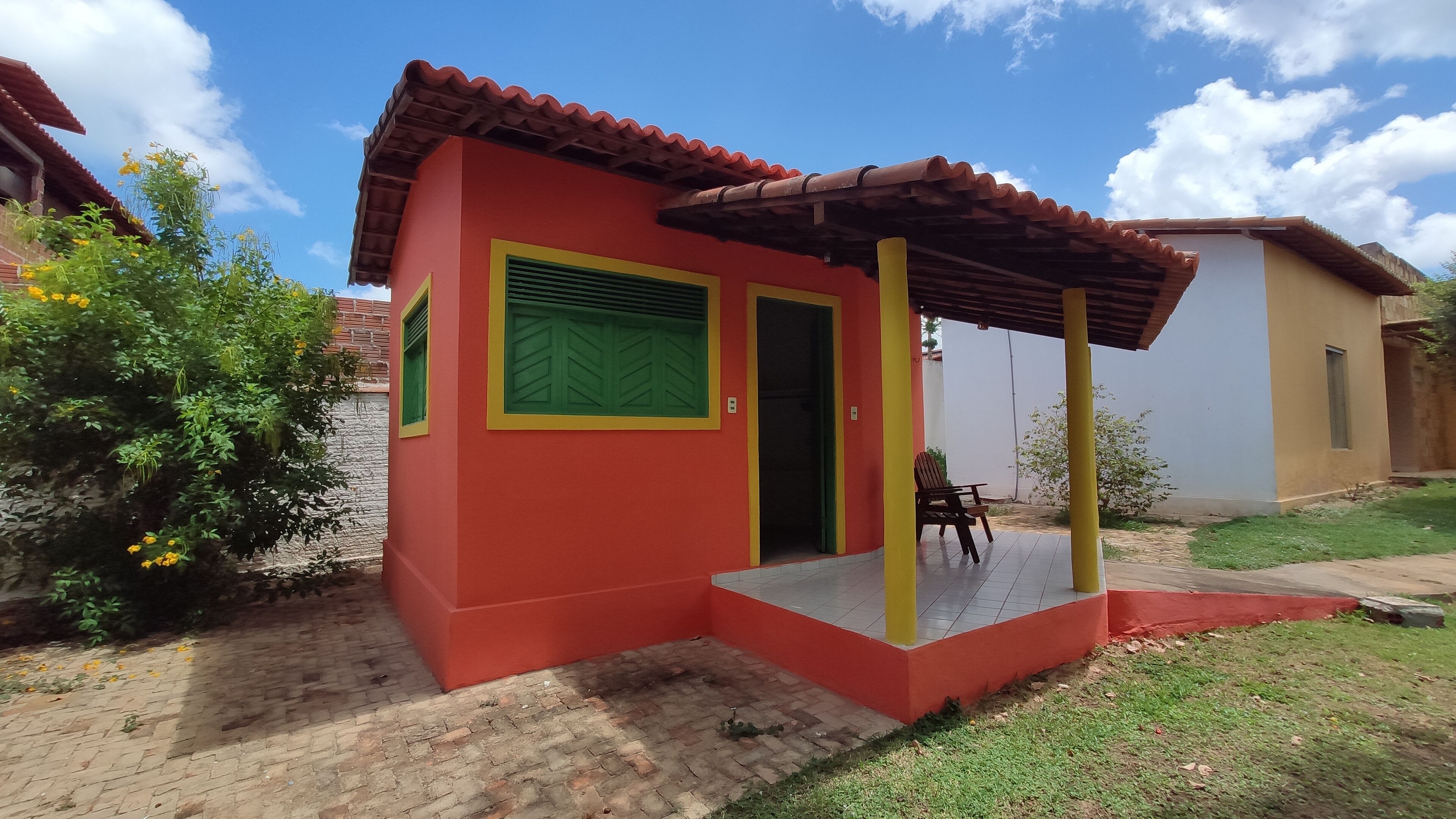 Un edificio pequeño de color rojo con un porche de baldosas y una puerta verde.