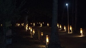 Ein beleuchteter Außenbereich bei Nacht mit gleichmäßig verteilten Laternen und einer zentralen Straßenlampe.