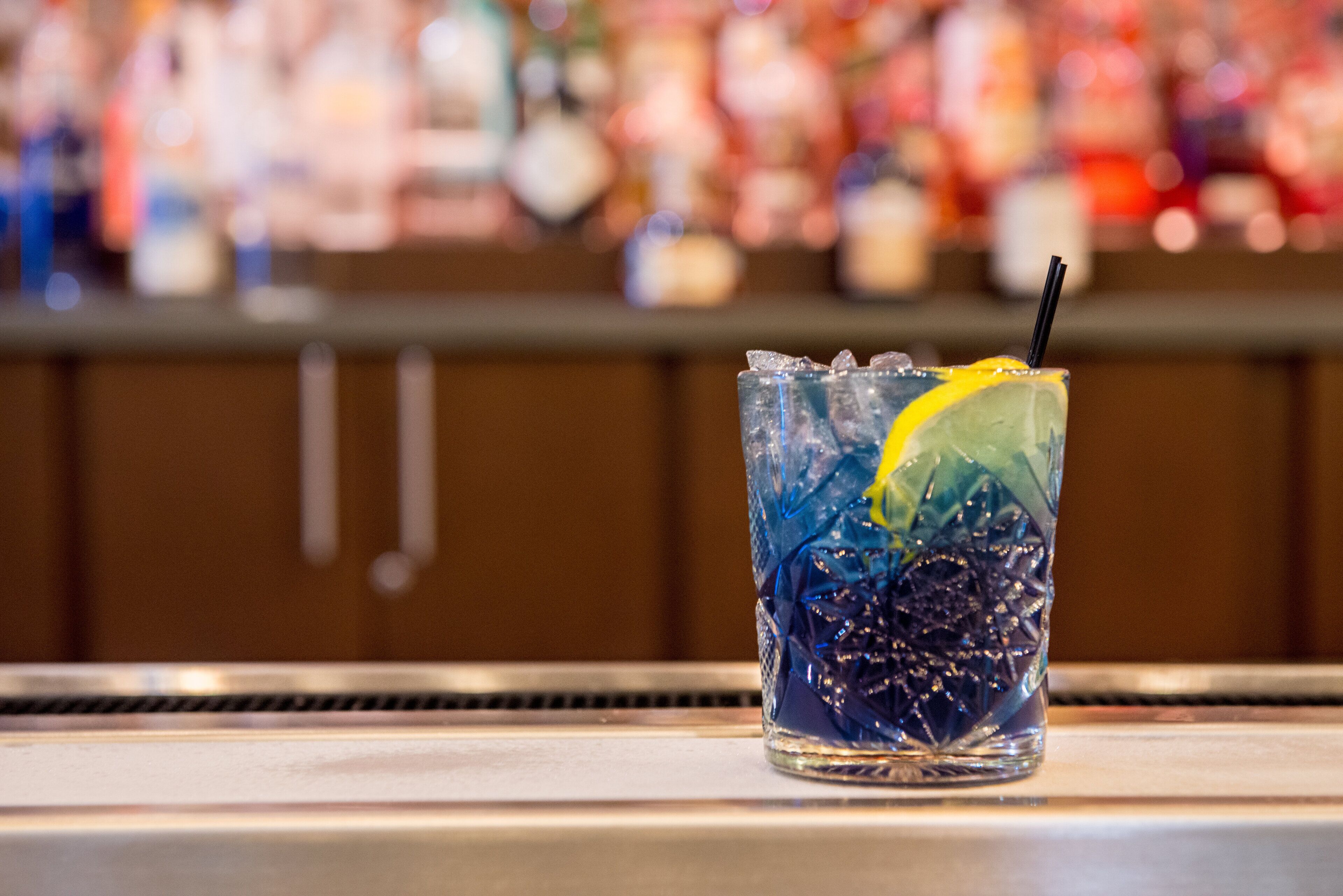 A glass with a straw and a lemon slice on a bar counter.