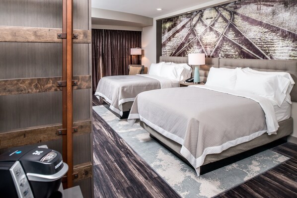 Une chambre d’hôtel avec deux lits, une grande fenêtre avec des rideaux, une œuvre d’art accrochée au mur et une petite table avec une lampe.