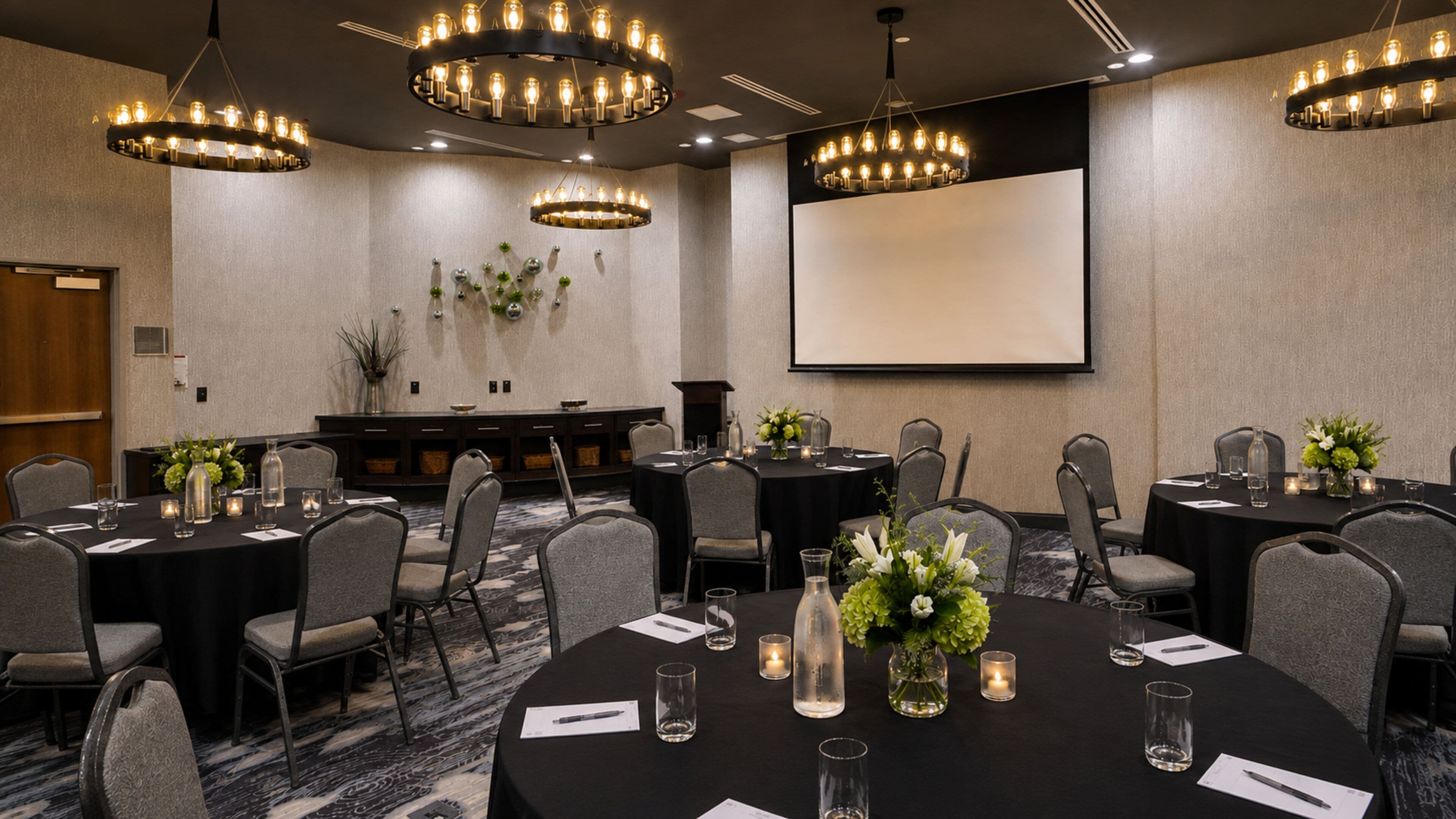 A conference room with round tables, chairs, and a projector screen.