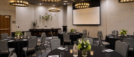 A conference room with round tables, chairs, and a projector screen.