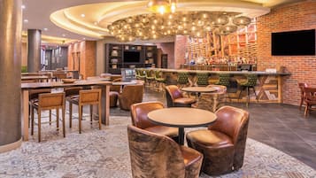Un restaurante con mesas y sillas redondas, una zona de bar y un suelo con estampado.