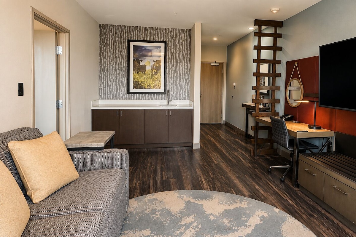A modern living room with a sofa, a coffee table, a TV, and a kitchen area with a dining table and chairs.