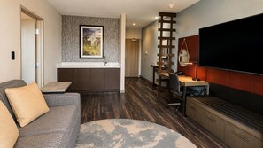A modern living room with a sofa, a coffee table, a TV, and a kitchen area with a dining table and chairs. - Hotel Indigo Frisco by IHG (Frisco)