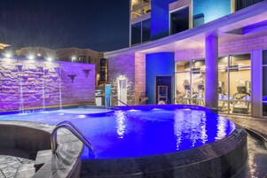 Una piscina al aire libre con un muro de piedra y un edificio moderno al fondo.