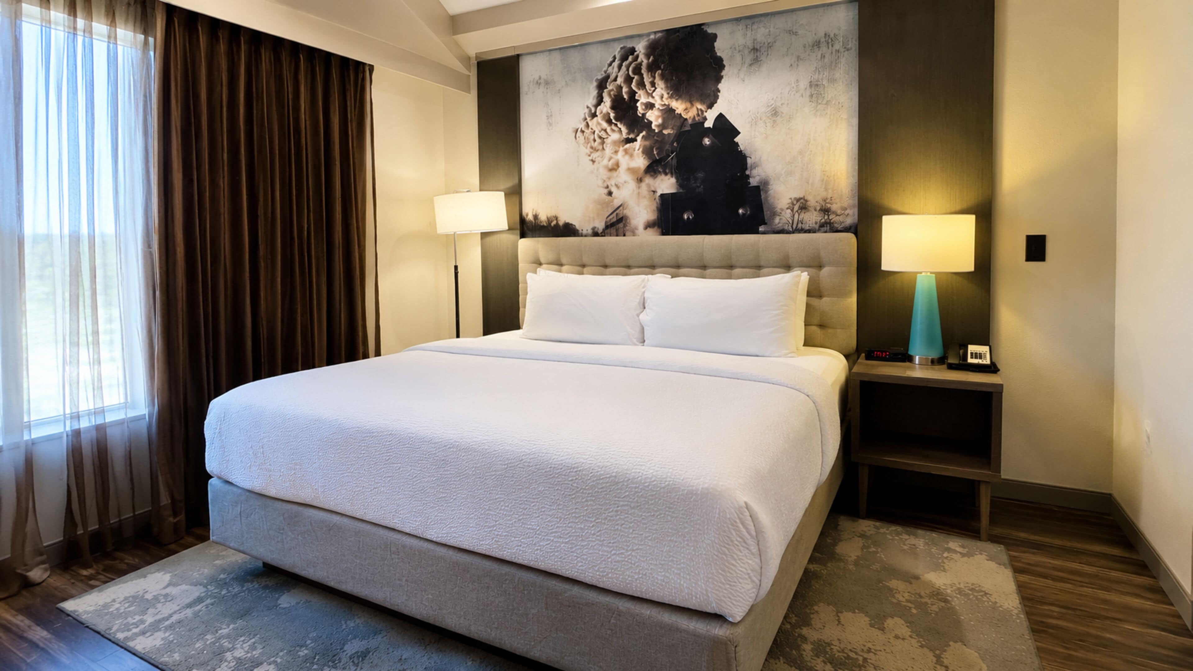 A hotel room with a large bed, two bedside lamps, a nightstand, and a painting on the wall.