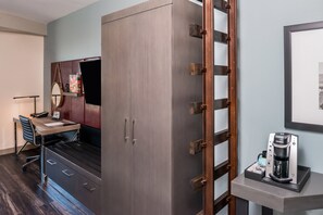 Une chambre de taille modeste comprenant un lit, un bureau avec une chaise, une armoire et une machine à café.