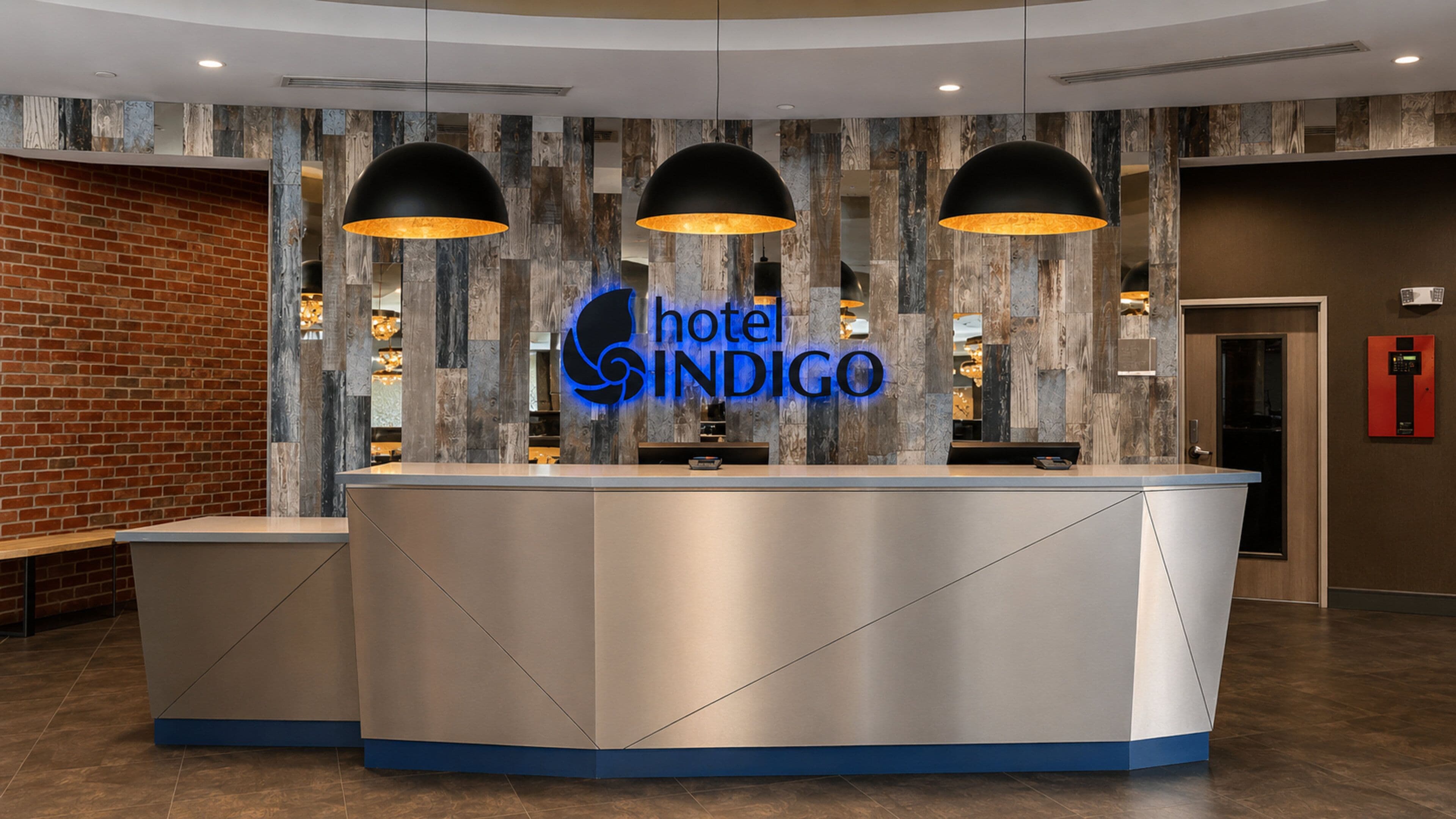 Un mostrador de recepción de hotel con diseño moderno, un logotipo y una zona de recepción con pared de ladrillo y paneles de madera.
