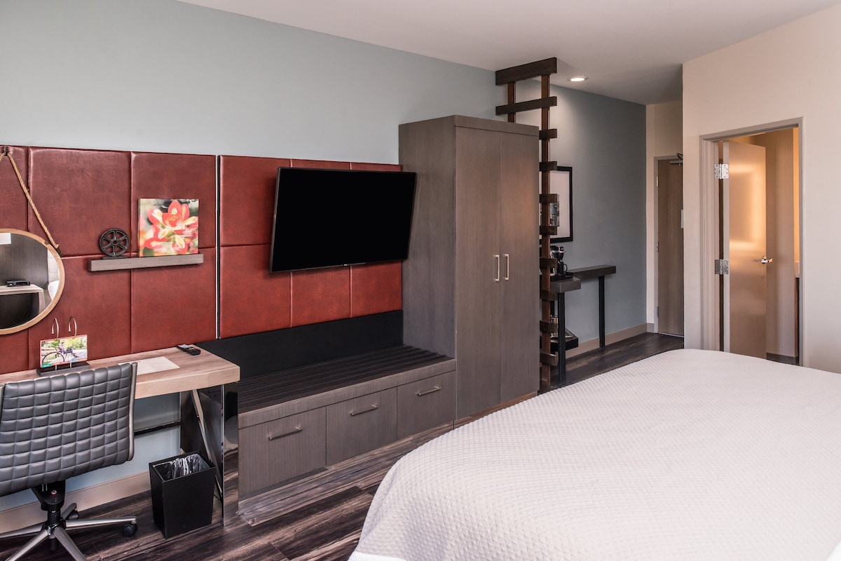 Moderni hotellihuone, jossa on sänky, työpöytä tuolilla, televisio ja vaatekaappi.