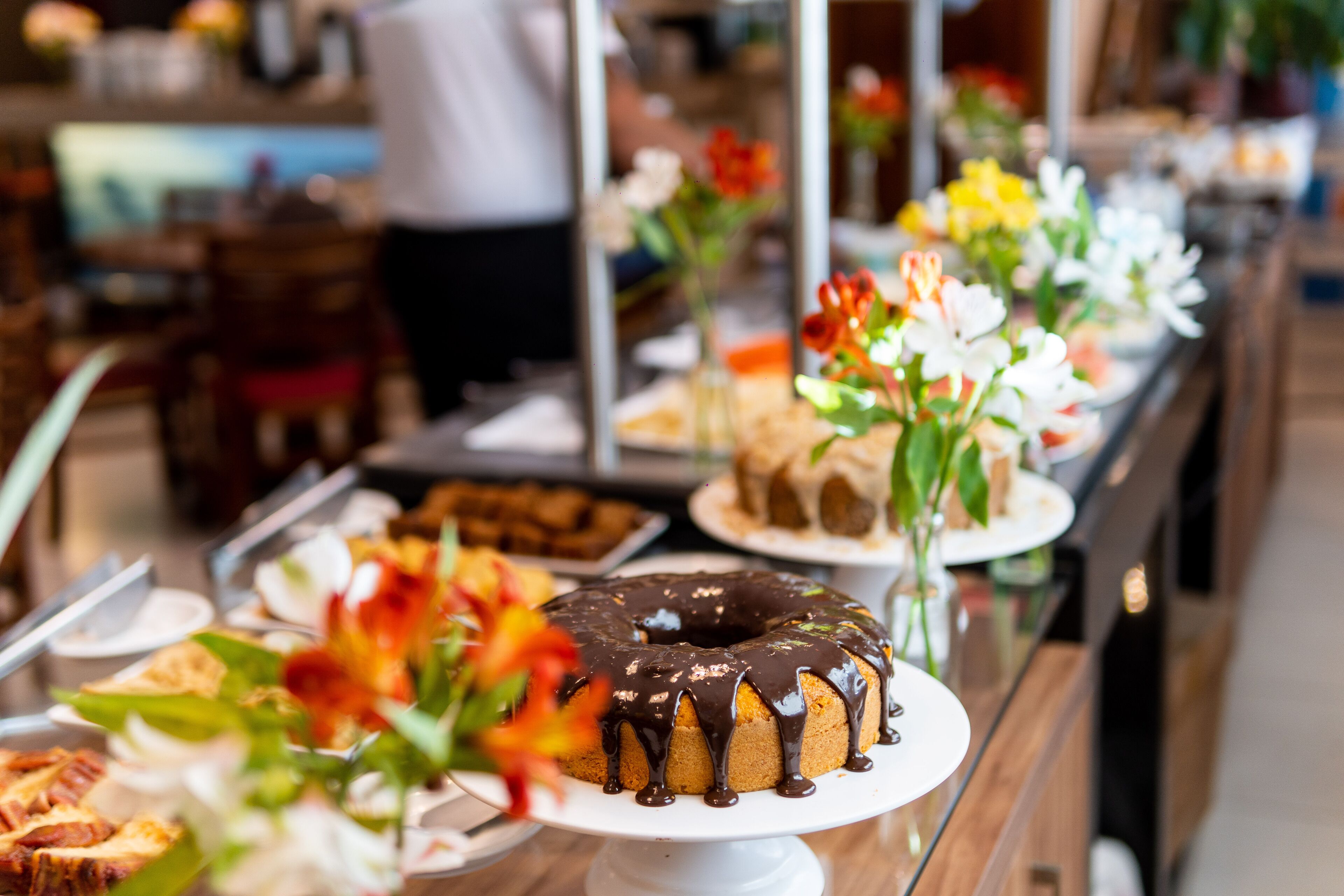 A buffet with various dishes and a chocolate-glazed cake on a white stand.