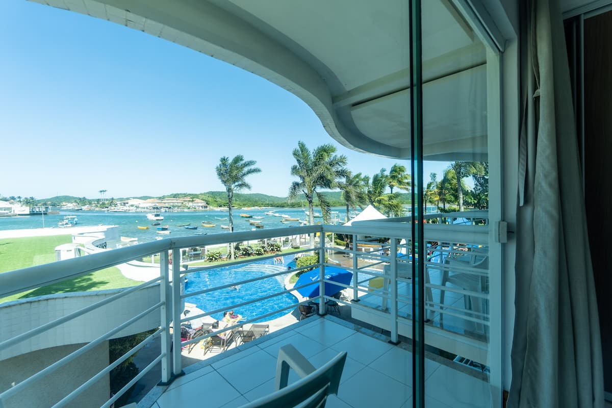Un balcón con vista a una piscina, sillones de descanso y un puerto deportivo lejano.
