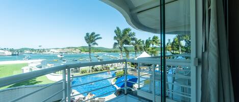 A balcony with a view of a swimming pool, lounge chairs, and a distant marina.