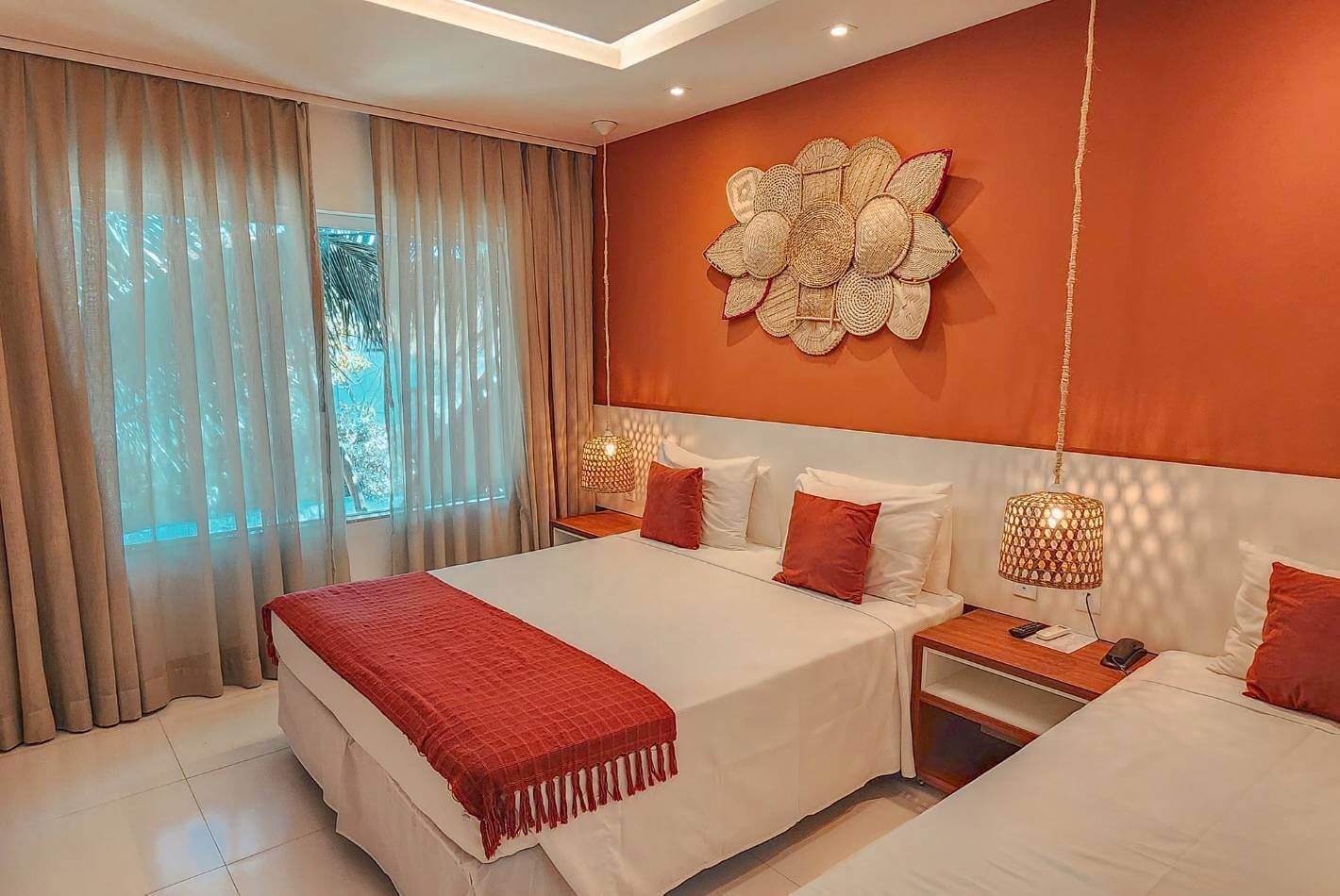 Quarto de hotel moderno com uma cama grande, duas mesas de cabeceira e um objeto decorativo na parede.