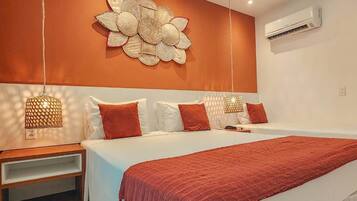 Un dormitorio moderno con una cama grande, ropa de cama blanca y un plaid rojo. Hay dos mesitas de noche con lámparas, y un aire acondicionado instalado en la pared.