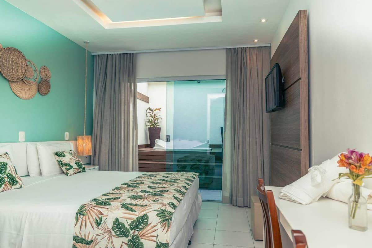 Habitación de hotel moderna con una cama grande, un escritorio, un televisor y un balcón con vistas.